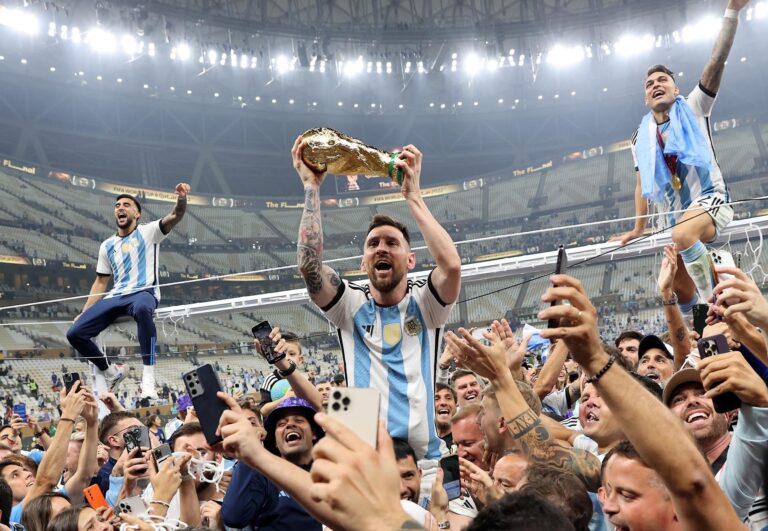 Grupo de personas con camisetas de la selección argentina observando un partido en una pantalla.