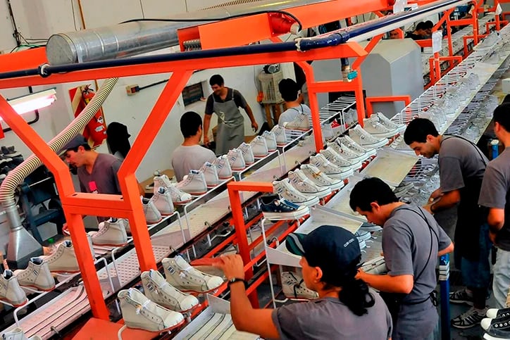 Gráfico que muestra una balanza comercial con íconos de fábrica y barco, representando el cambio de producción local a importaciones.