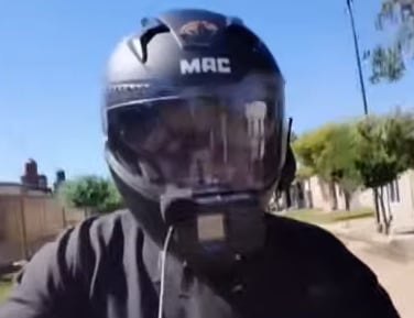 Fotograma del video donde se ve a un joven intentando arrebatar un celular a un hombre que conduce una moto en una calle de tierra.