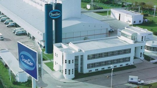 Logotipo de la cooperativa láctea SanCor sobre un fondo relacionado con la industria alimentaria argentina.