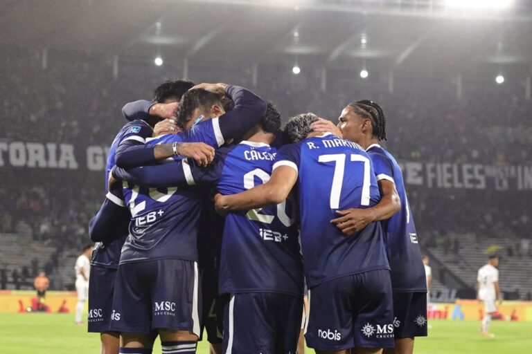 Jugadores de Talleres y Riestra en el campo del estadio Mario Alberto Kempes, con el césped mojado tras la lluvia.