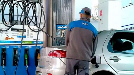 Persona cargando combustible en una estación de servicio, con surtidores de nafta y gasoil visibles